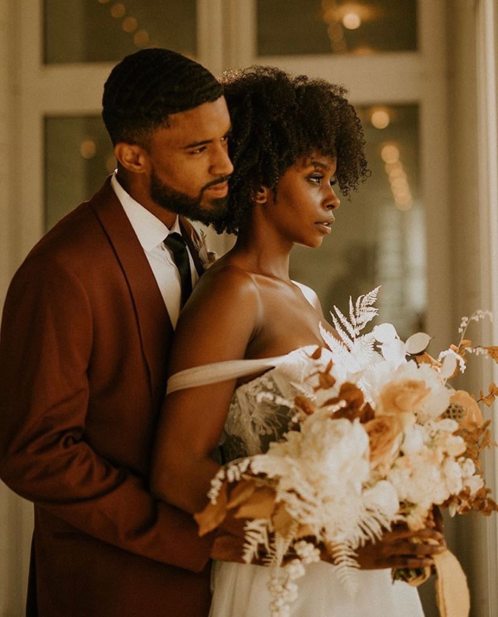 Abyon Ausar in a burgundy suit with a bride and gold floral styling