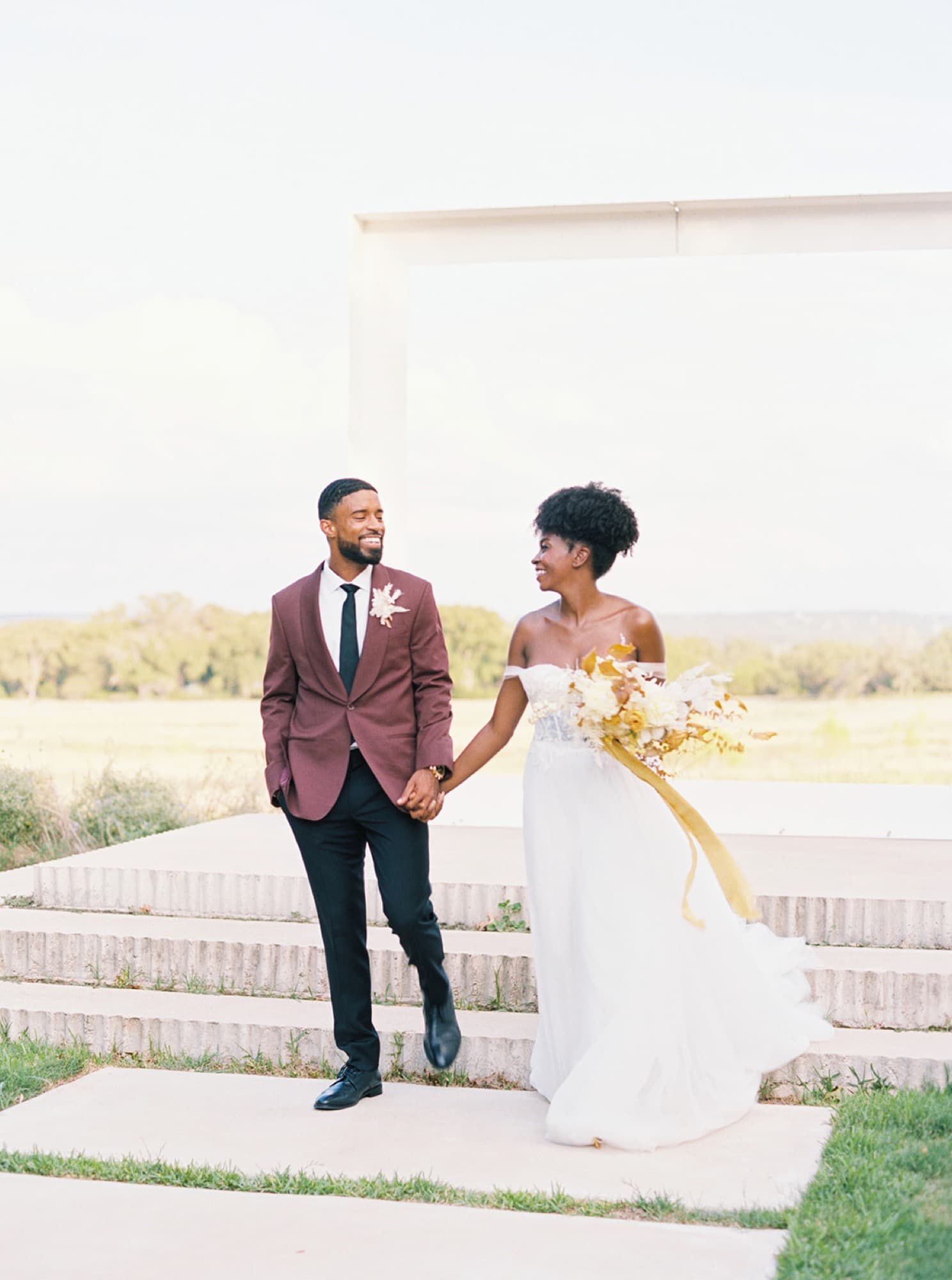 Abyon Ausar in a burgundy suit with a bride outdoors at golden hour