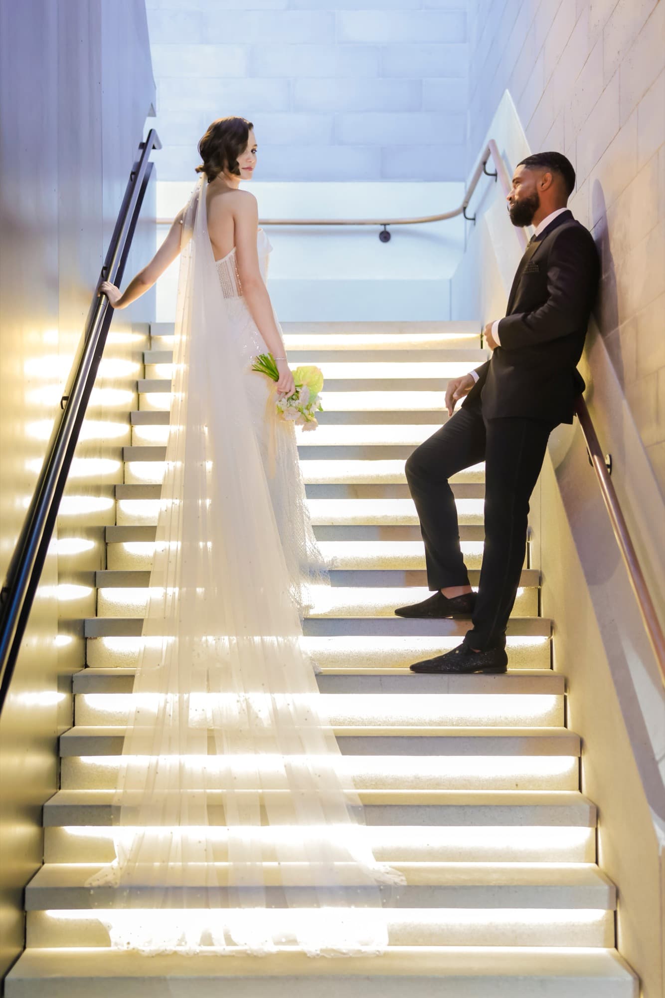 Abyon Ausar in black tie with a bride on a lit staircase
