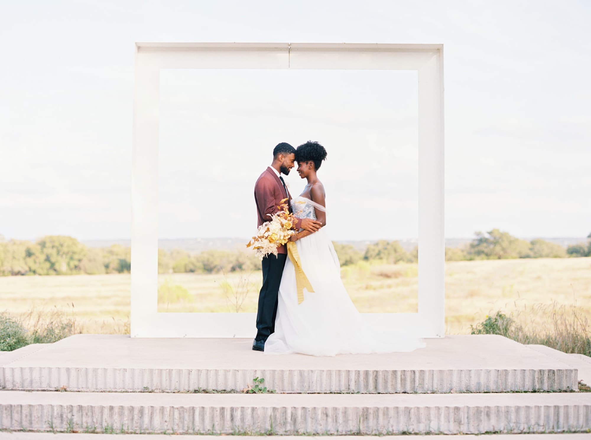Abyon Ausar with a bride framed by a ceremony arch in an open field