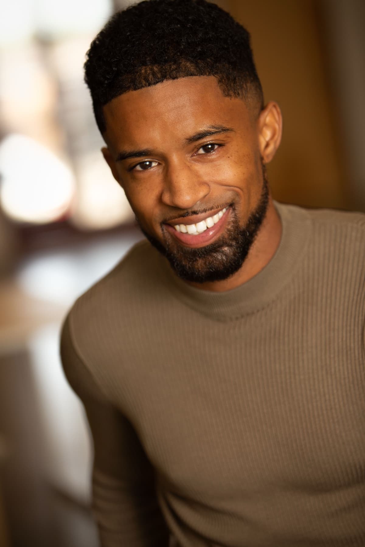 Smiling close headshot of Abyon Ausar in a tan sweater