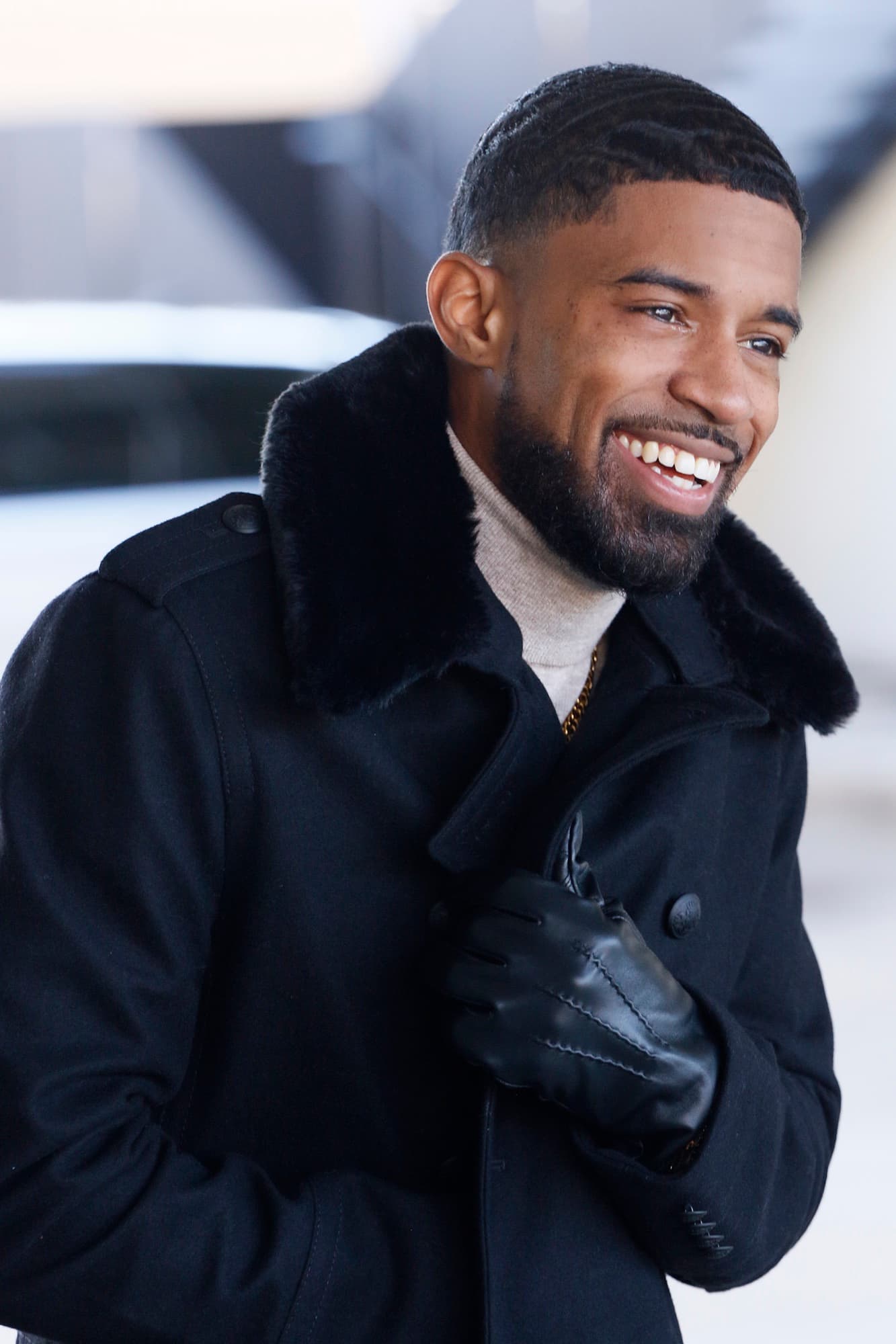 Smiling photo of Abyon Ausar walking outdoors in a black peacoat and leather gloves