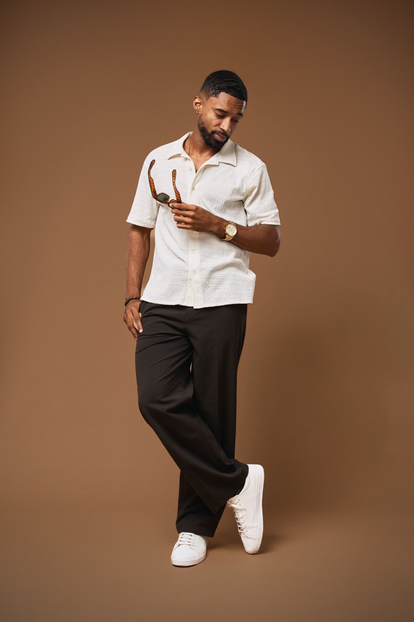 Abyon Ausar in a cream camp shirt and dark trousers, holding sunglasses