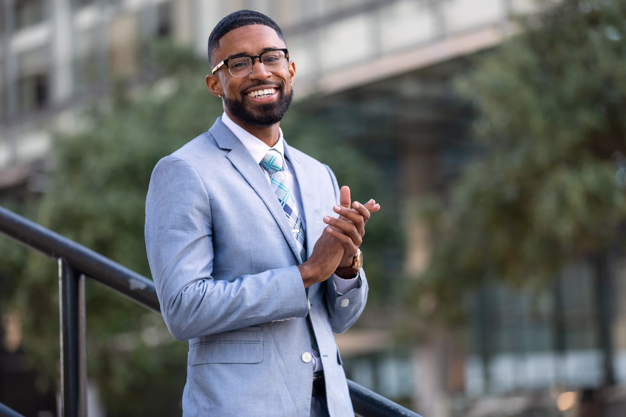Abyon Ausar in a light grey suit and glasses, smiling outdoors