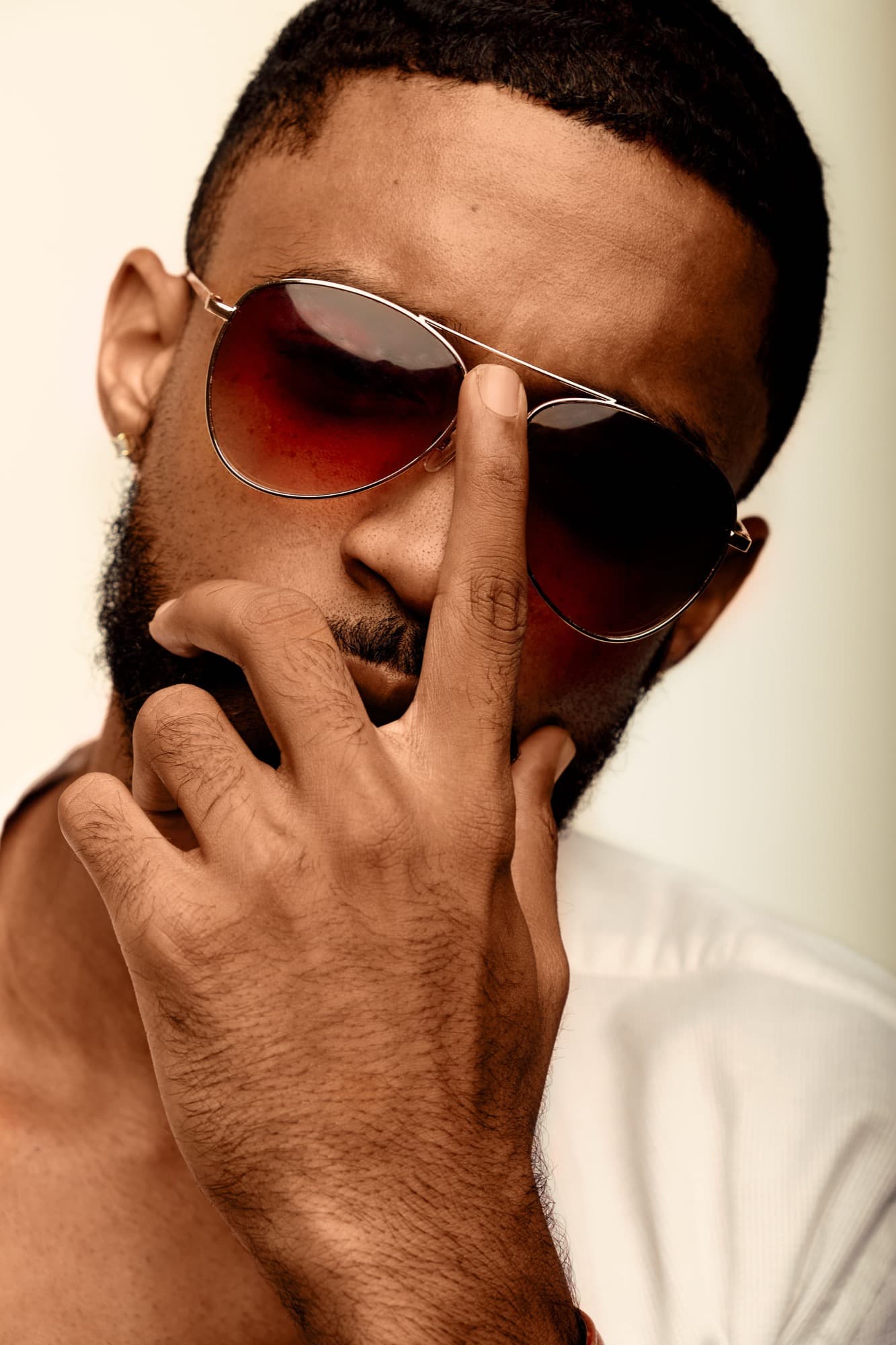 Abyon Ausar in sunglasses and a white shirt, hand raised to his face, warm light