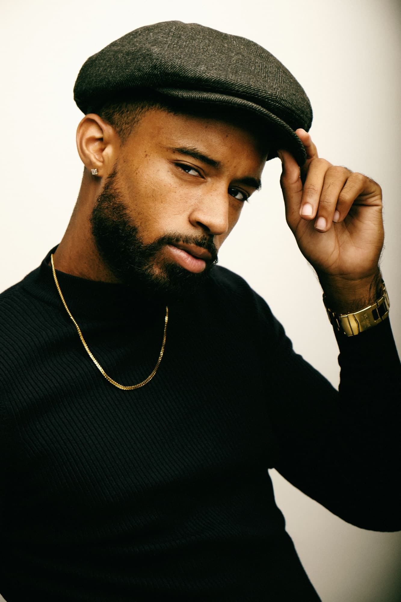 Abyon Ausar in a flat cap and black turtleneck with a gold chain