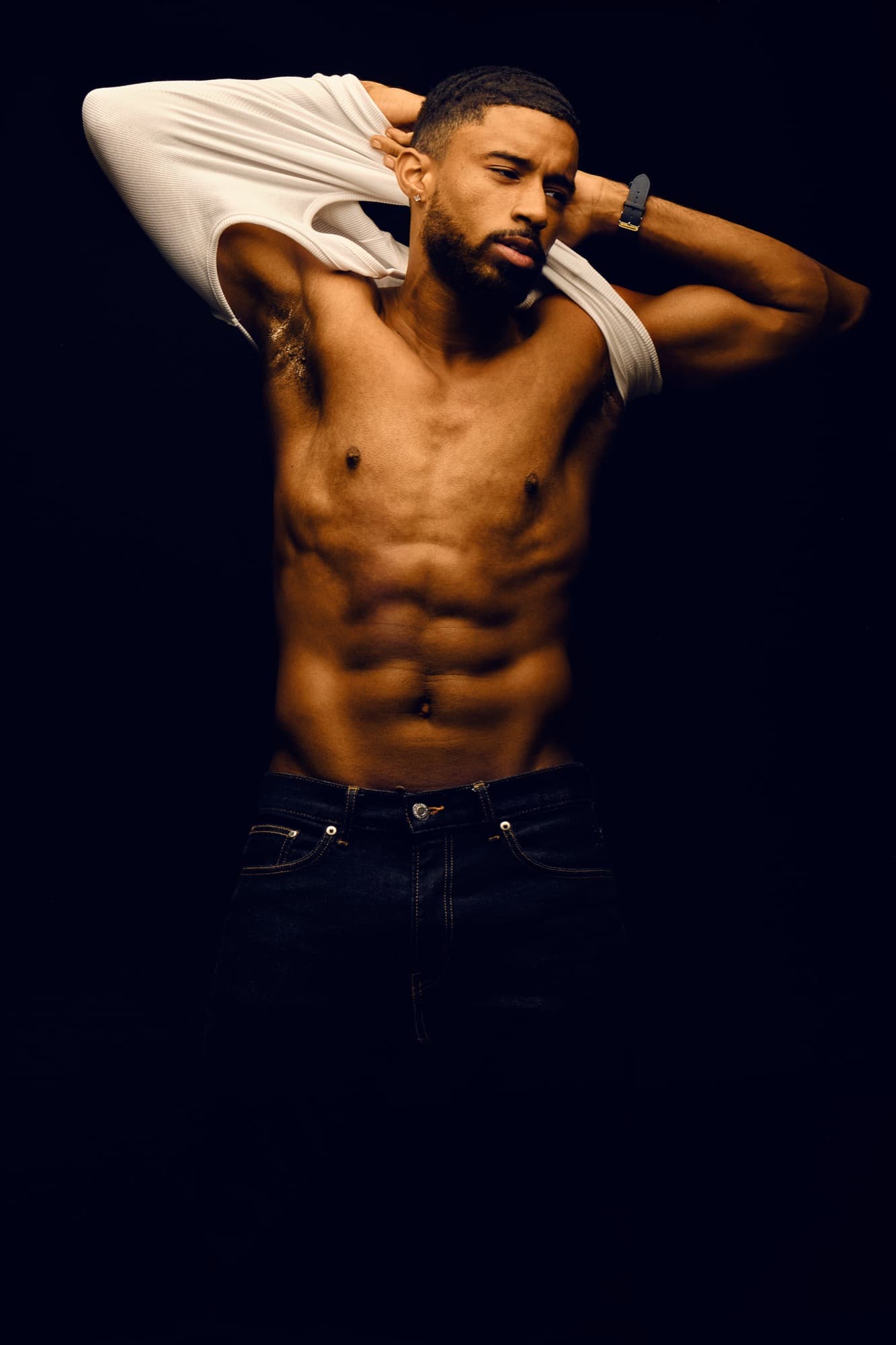 Physique studio shot of Abyon Ausar, arm raised, against a blue backdrop