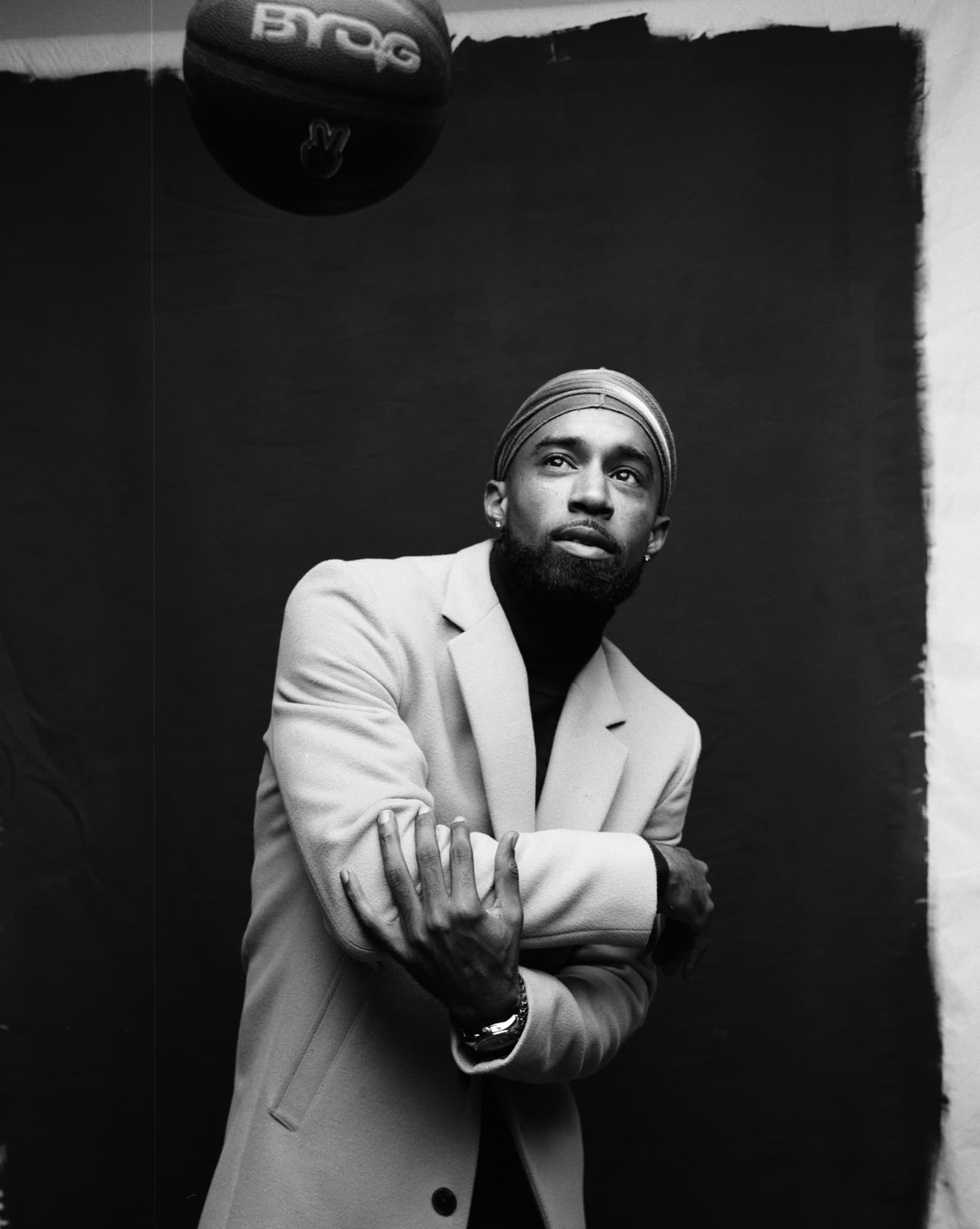 Black and white portrait of Abyon Ausar in a tailored overcoat with a basketball above him