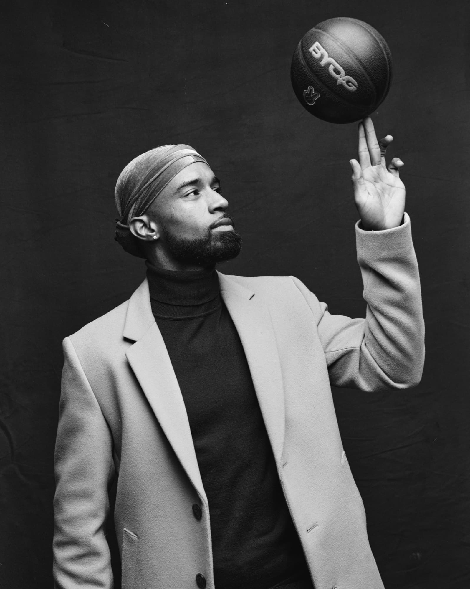 Black and white portrait of Abyon Ausar in an overcoat spinning a basketball on one finger