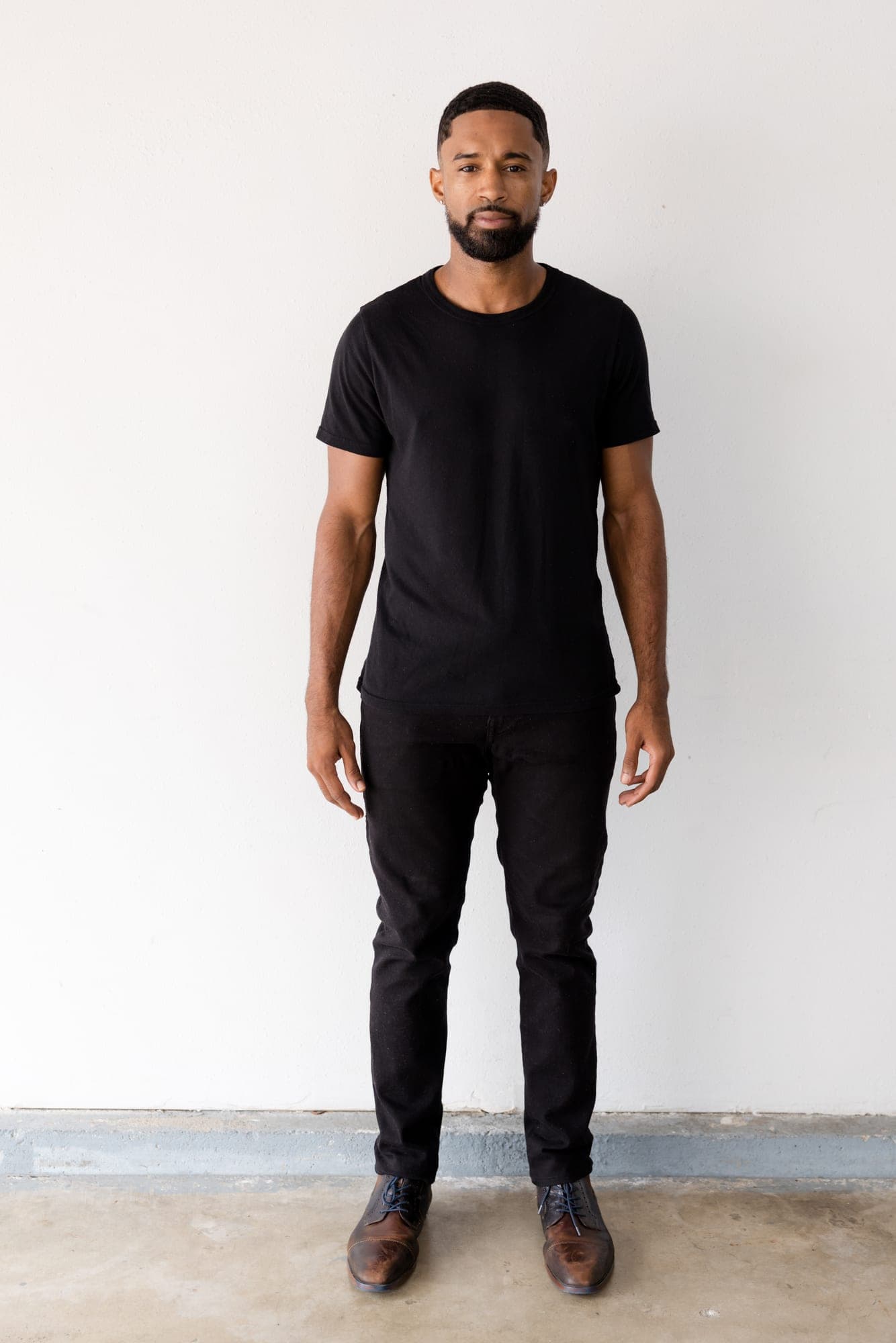 Full length digital of Abyon Ausar in a black tee and black jeans against a white wall